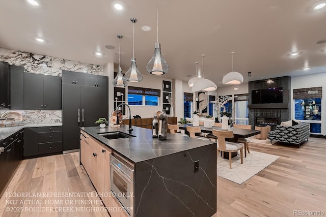 kitchen with sink, decorative light fixtures, a large fireplace, a kitchen island with sink, and decorative backsplash