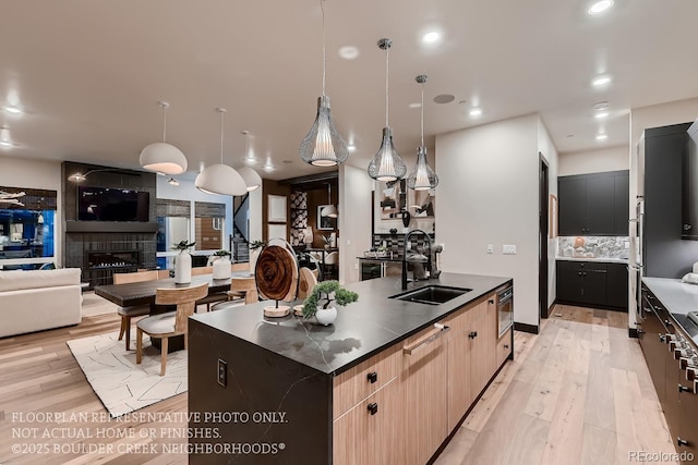 kitchen with sink, decorative light fixtures, light hardwood / wood-style flooring, a center island with sink, and light brown cabinets