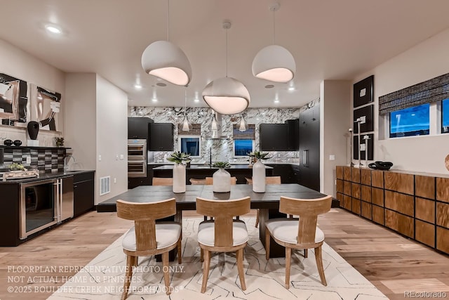 kitchen with stainless steel double oven, beverage cooler, decorative backsplash, and light hardwood / wood-style flooring