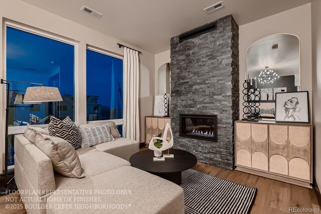 living room with hardwood / wood-style flooring, a stone fireplace, and a chandelier