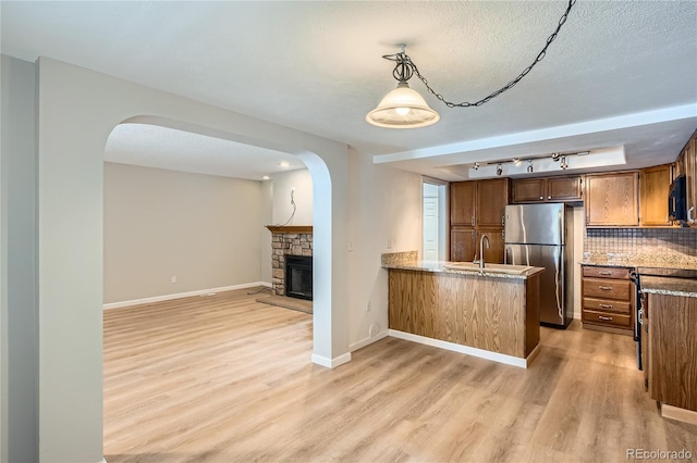 kitchen featuring a stone fireplace, stainless steel fridge, tasteful backsplash, decorative light fixtures, and kitchen peninsula