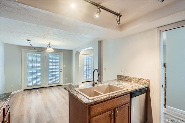 kitchen featuring sink, rail lighting, stainless steel dishwasher, light hardwood / wood-style floors, and a textured ceiling