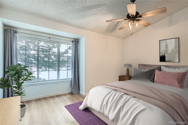 bedroom featuring ceiling fan, light hardwood / wood-style floors, lofted ceiling, and a textured ceiling