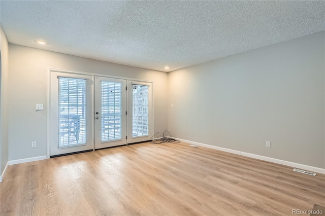 empty room with a textured ceiling and light hardwood / wood-style flooring