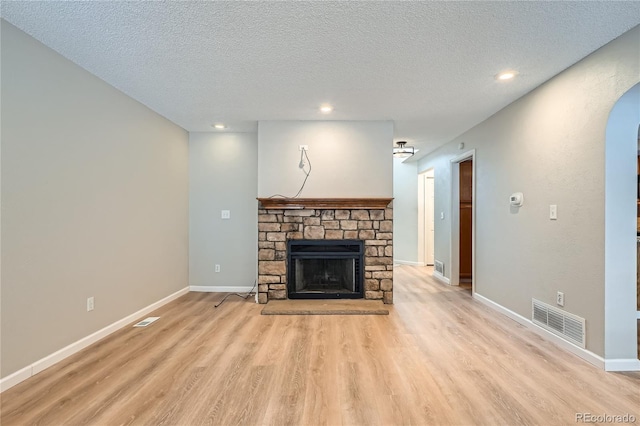 unfurnished living room featuring light wood-type flooring, a textured ceiling, and a stone fireplace