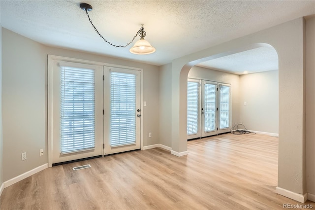 doorway with a textured ceiling, light hardwood / wood-style flooring, and plenty of natural light