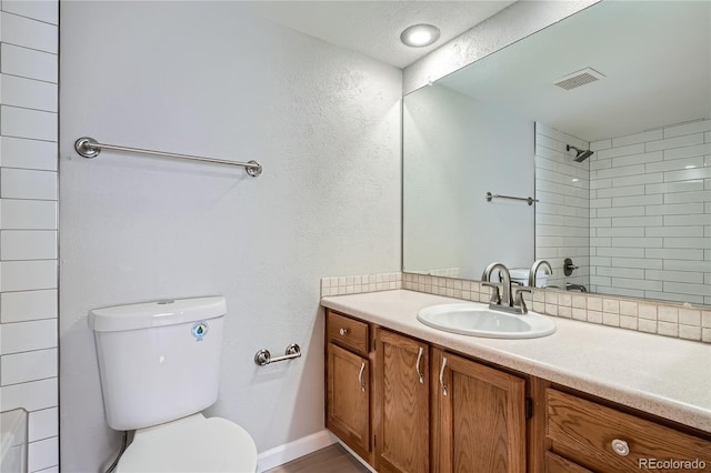 bathroom featuring tiled shower, vanity, and toilet