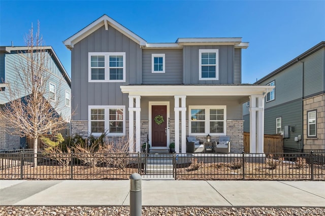 view of front of home featuring board and batten siding, covered porch, a fenced front yard, and stone siding