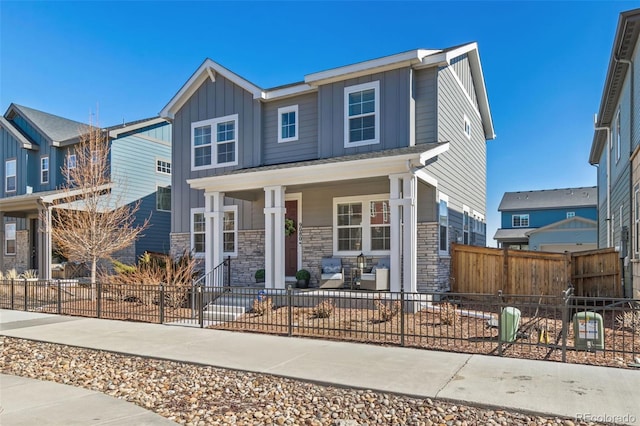 view of front of home with covered porch, stone siding, board and batten siding, and a fenced front yard