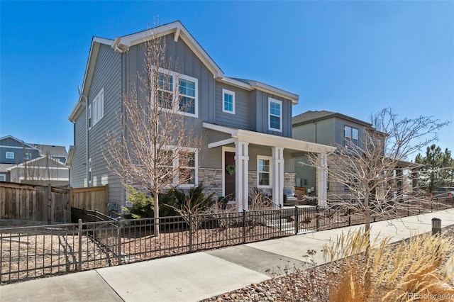 view of front of property with stone siding, a fenced front yard, covered porch, and board and batten siding