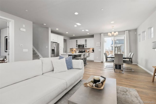 living area with baseboards, a notable chandelier, light wood-style flooring, and recessed lighting