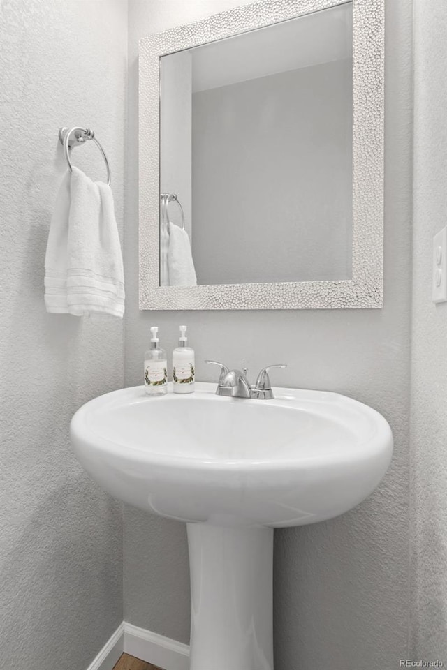 bathroom with a textured wall, a sink, and baseboards