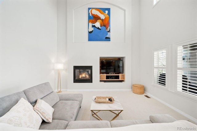 living room with carpet floors, baseboards, a high ceiling, and a glass covered fireplace