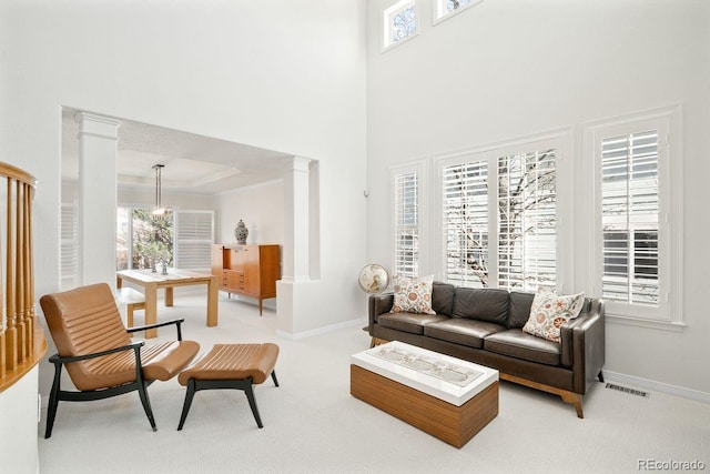 living area featuring visible vents, ornate columns, and light carpet