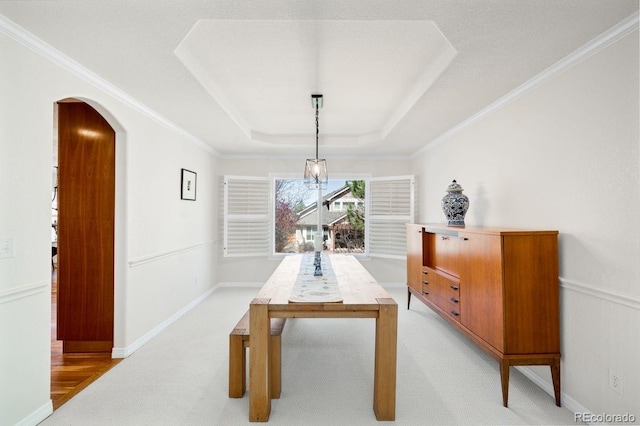 dining space featuring a tray ceiling, arched walkways, light colored carpet, ornamental molding, and baseboards