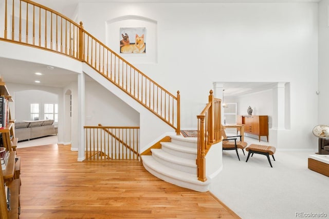 staircase with arched walkways, a high ceiling, baseboards, and wood finished floors