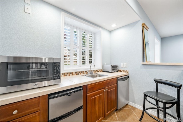 kitchen featuring dishwasher, a sink, brown cabinetry, fridge, and decorative backsplash