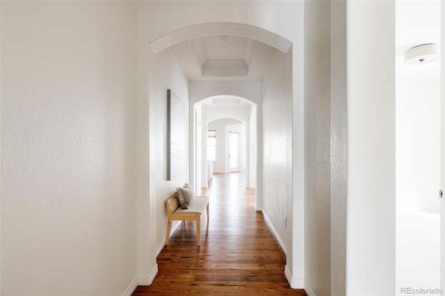 hallway featuring a raised ceiling, ornamental molding, and dark wood-type flooring