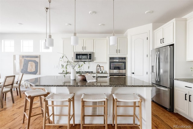 kitchen with a kitchen island with sink, hanging light fixtures, white cabinetry, and appliances with stainless steel finishes