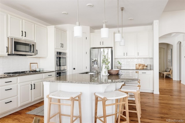 kitchen featuring stainless steel appliances, a kitchen island with sink, sink, and white cabinets