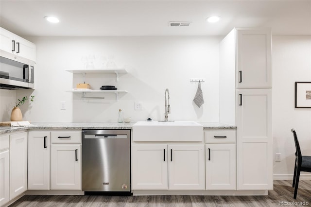 kitchen with appliances with stainless steel finishes, white cabinetry, sink, hardwood / wood-style flooring, and light stone countertops