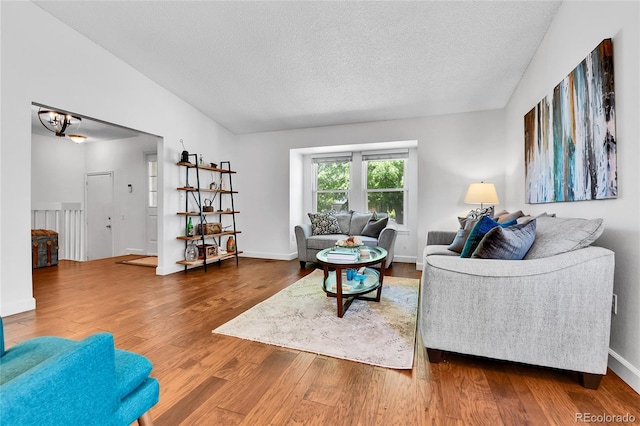 living room featuring a textured ceiling, wood finished floors, vaulted ceiling, a chandelier, and baseboards