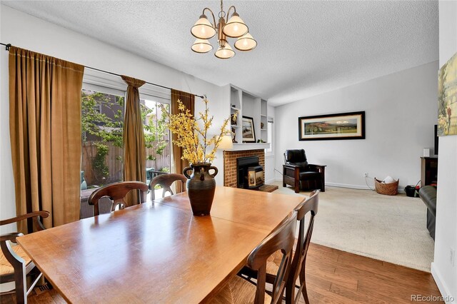 dining area with a brick fireplace, a textured ceiling, a chandelier, wood finished floors, and baseboards