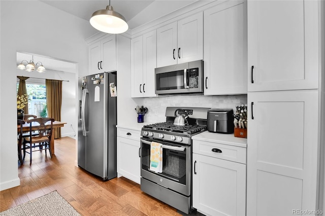 kitchen with appliances with stainless steel finishes, light countertops, backsplash, light wood finished floors, and white cabinets