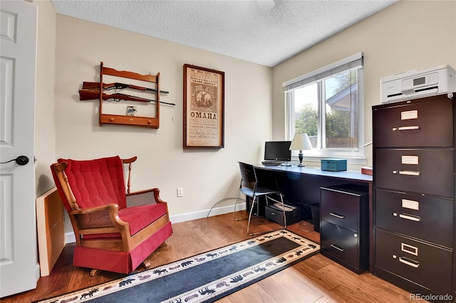 office featuring light wood-type flooring, a textured ceiling, and baseboards