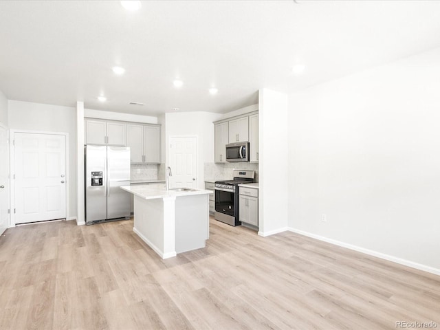 kitchen with backsplash, a kitchen island with sink, sink, light hardwood / wood-style floors, and stainless steel appliances