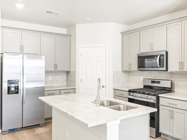 kitchen with light stone counters, a kitchen island with sink, light hardwood / wood-style flooring, sink, and stainless steel appliances