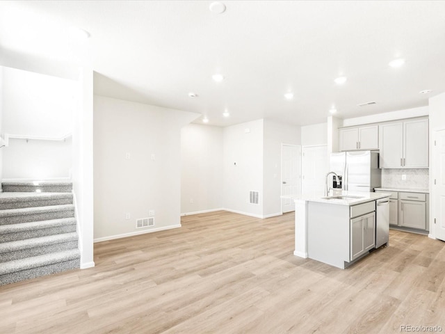 kitchen with gray cabinets, an island with sink, stainless steel appliances, and light hardwood / wood-style floors