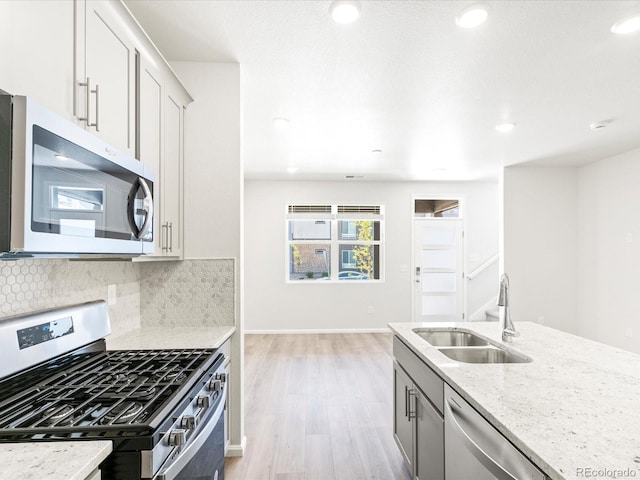 kitchen with decorative backsplash, light hardwood / wood-style flooring, stainless steel appliances, sink, and light stone counters