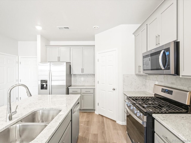 kitchen featuring decorative backsplash, appliances with stainless steel finishes, light stone countertops, light hardwood / wood-style floors, and sink