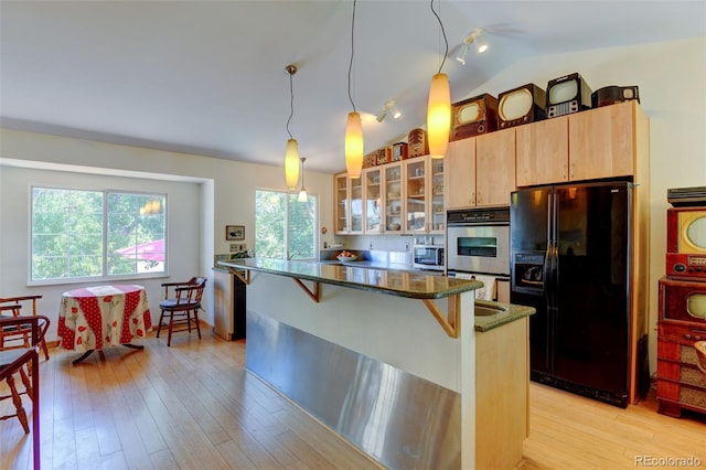 kitchen with a breakfast bar, light brown cabinetry, appliances with stainless steel finishes, pendant lighting, and dark stone counters