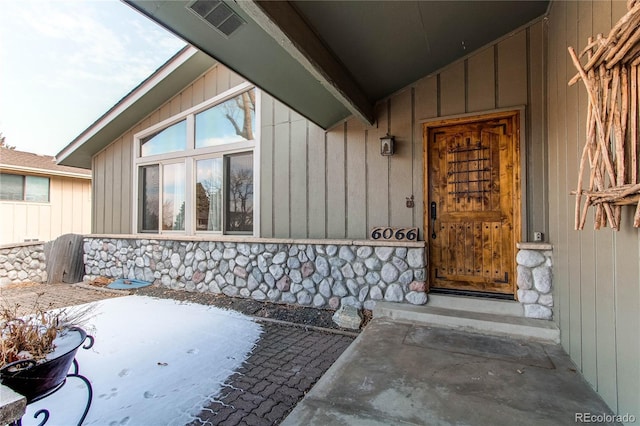 view of exterior entry with stone siding, board and batten siding, and visible vents