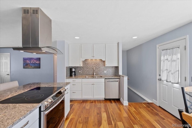 kitchen with a sink, wall chimney exhaust hood, appliances with stainless steel finishes, and white cabinets