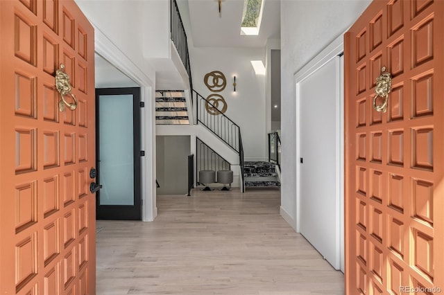 entrance foyer with stairway, light wood-type flooring, a skylight, and a high ceiling