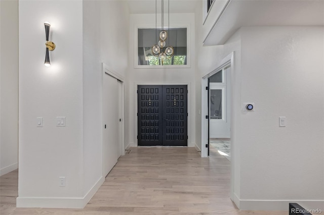 entryway featuring light wood-style flooring, baseboards, a chandelier, and a towering ceiling