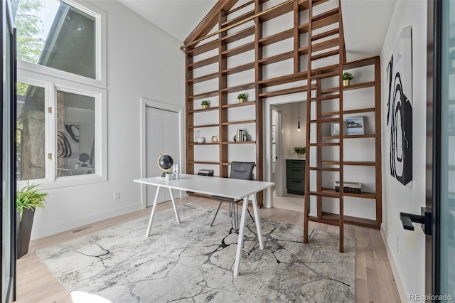 home office featuring light wood finished floors, high vaulted ceiling, and baseboards