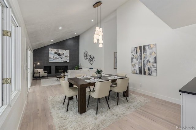dining area with light wood-style flooring, high vaulted ceiling, a large fireplace, plenty of natural light, and baseboards