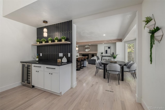 dining room with a bar, beverage cooler, light wood-style floors, and baseboards