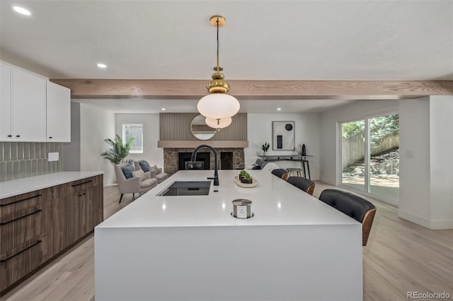 kitchen with open floor plan, a stone fireplace, light wood finished floors, a sink, and light countertops