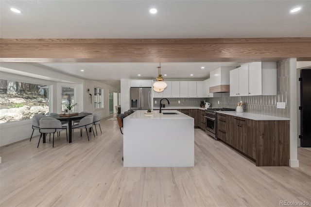 kitchen featuring appliances with stainless steel finishes, a sink, wall chimney exhaust hood, white cabinetry, and beamed ceiling