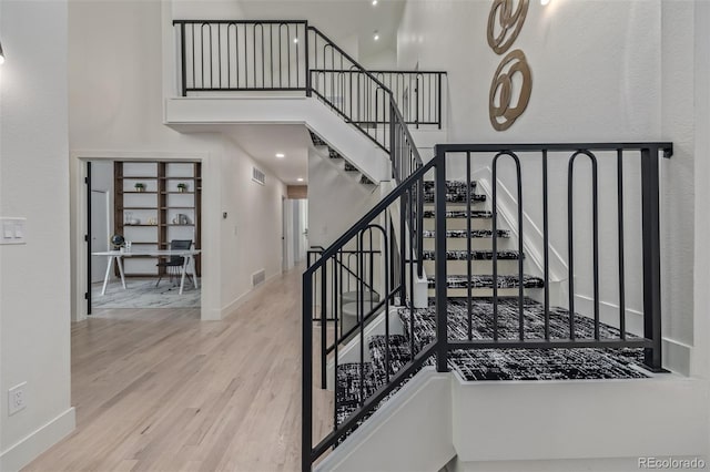 staircase with wood finished floors, a high ceiling, and baseboards