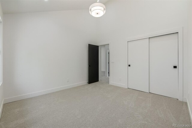 unfurnished bedroom with carpet floors, high vaulted ceiling, a closet, and baseboards