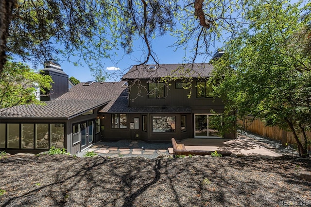 rear view of house with a chimney, fence, a deck, a shingled roof, and a patio