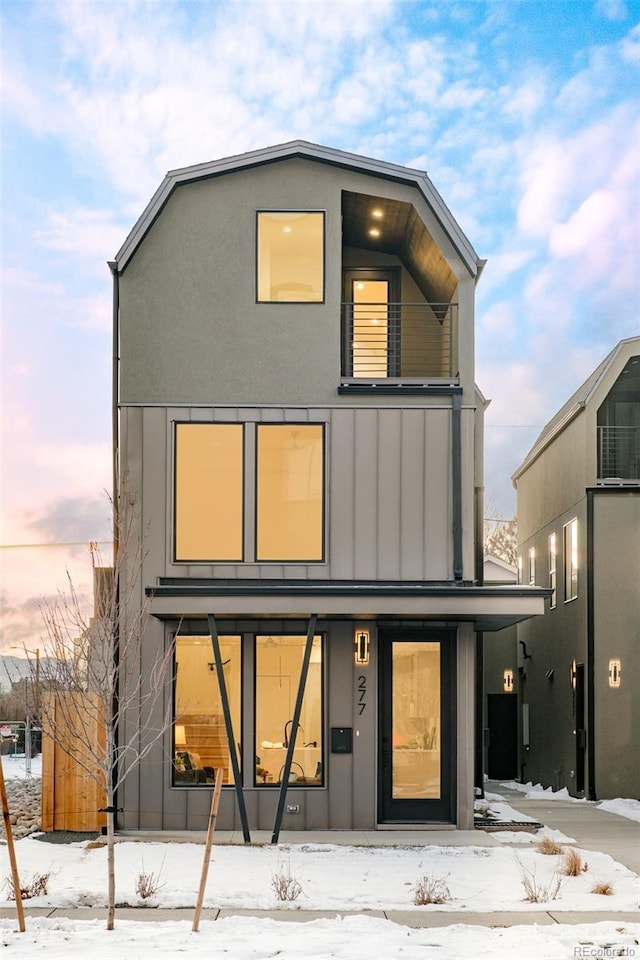 snow covered back of property featuring board and batten siding and a balcony