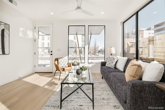 living room featuring ceiling fan, light wood finished floors, visible vents, and baseboards