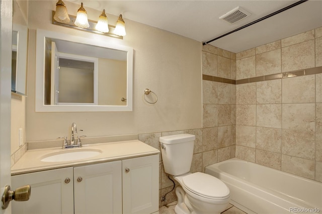 full bathroom with tile patterned flooring, tiled shower / bath, toilet, vanity, and tile walls